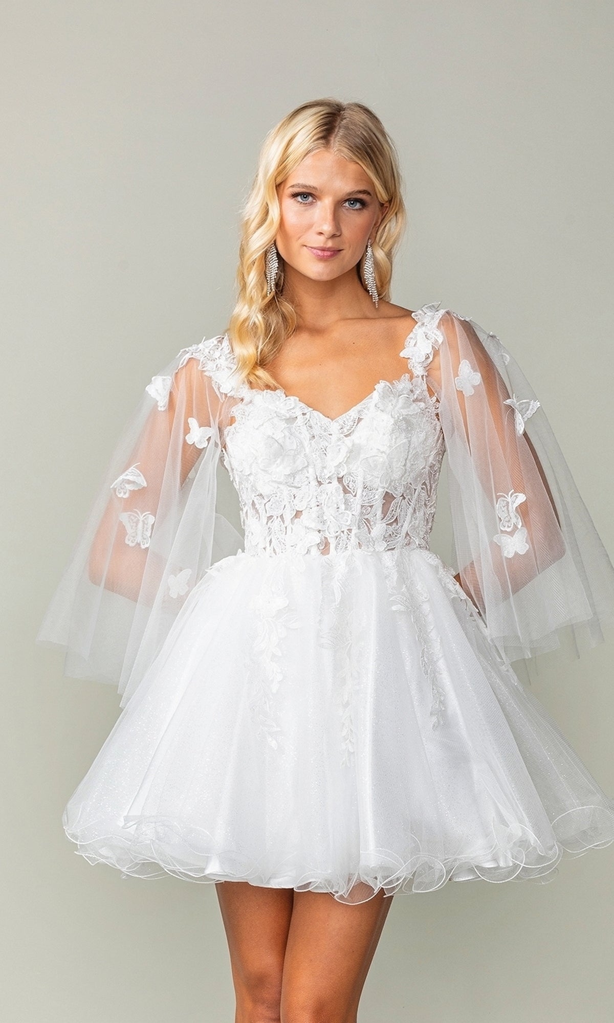 A woman wears the Butterfly-Cape Short A-Line Homecoming Dress 3393, featuring a white design with sheer puff sleeves, floral lace, and sequin appliques, standing against a plain light background.